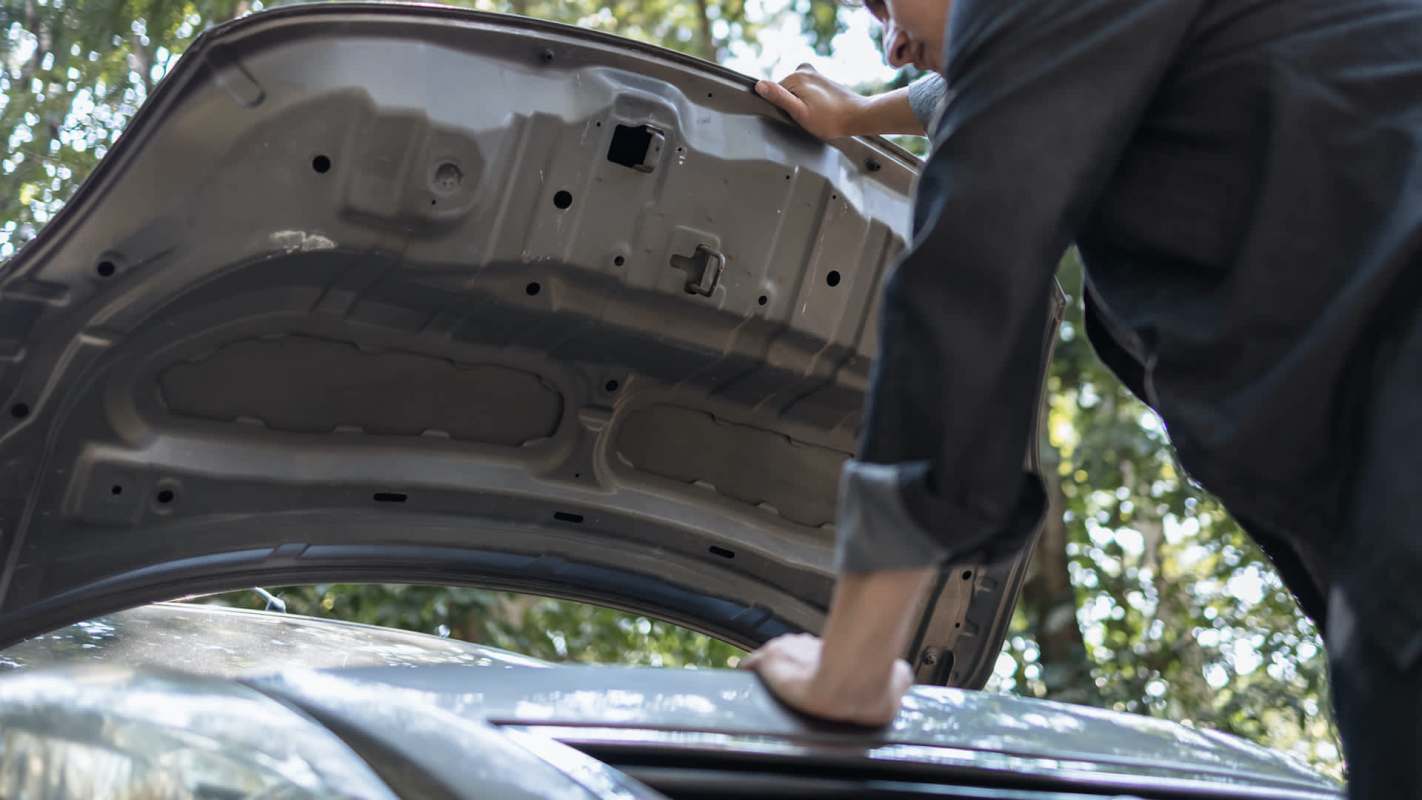 A person inspects the engine of a car with the hood raised.