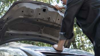 A person inspects the engine of a car with the hood raised.