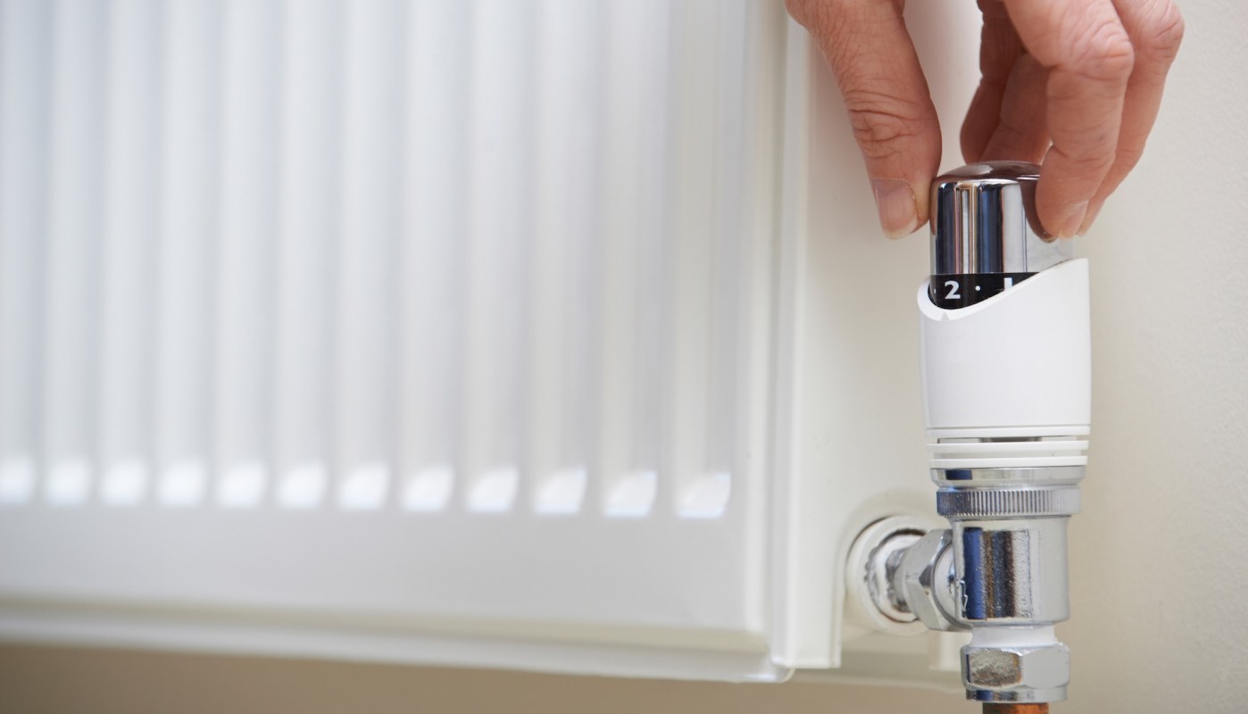 A hand adjusts the temperature dial on a radiator valve.