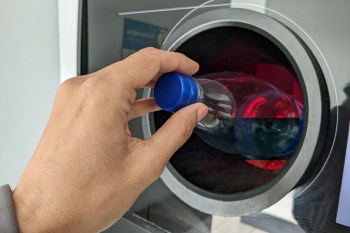 A hand places a plastic bottle into a recycling machine.