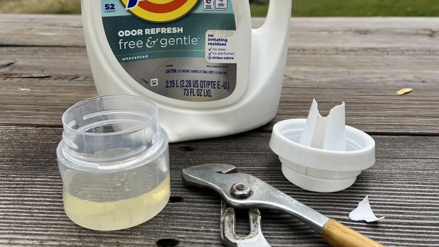 A bottle of laundry detergent, a small container, a broken cap, and a pair of pliers on a wooden surface.