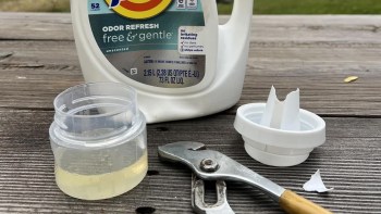 A bottle of laundry detergent, a small container, a broken cap, and a pair of pliers on a wooden surface.