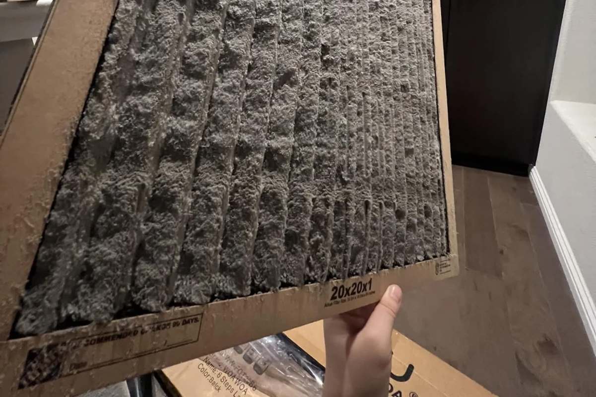 A person holds a dirty air filter with visible dust and debris.