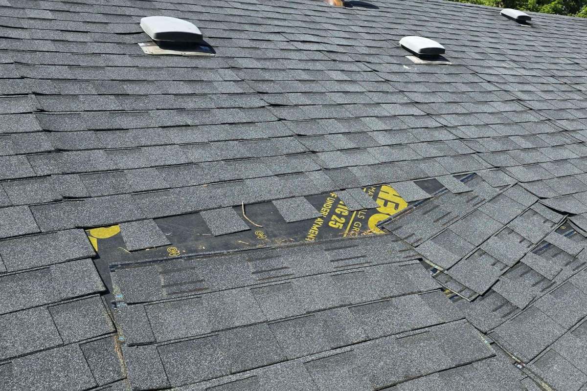 A section of a roof with overlapping gray shingles, showing some wear and a yellow marked underlayment.