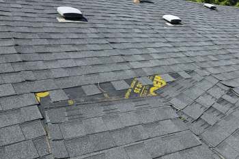 A section of a roof with overlapping gray shingles, showing some wear and a yellow marked underlayment.