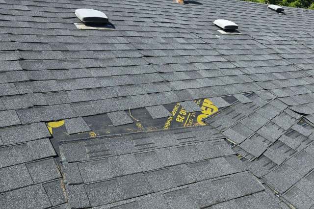 A section of a roof with overlapping gray shingles, showing some wear and a yellow marked underlayment.