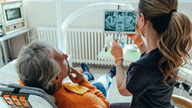 A dentist shows an X-ray to an older male patient in a dental office.