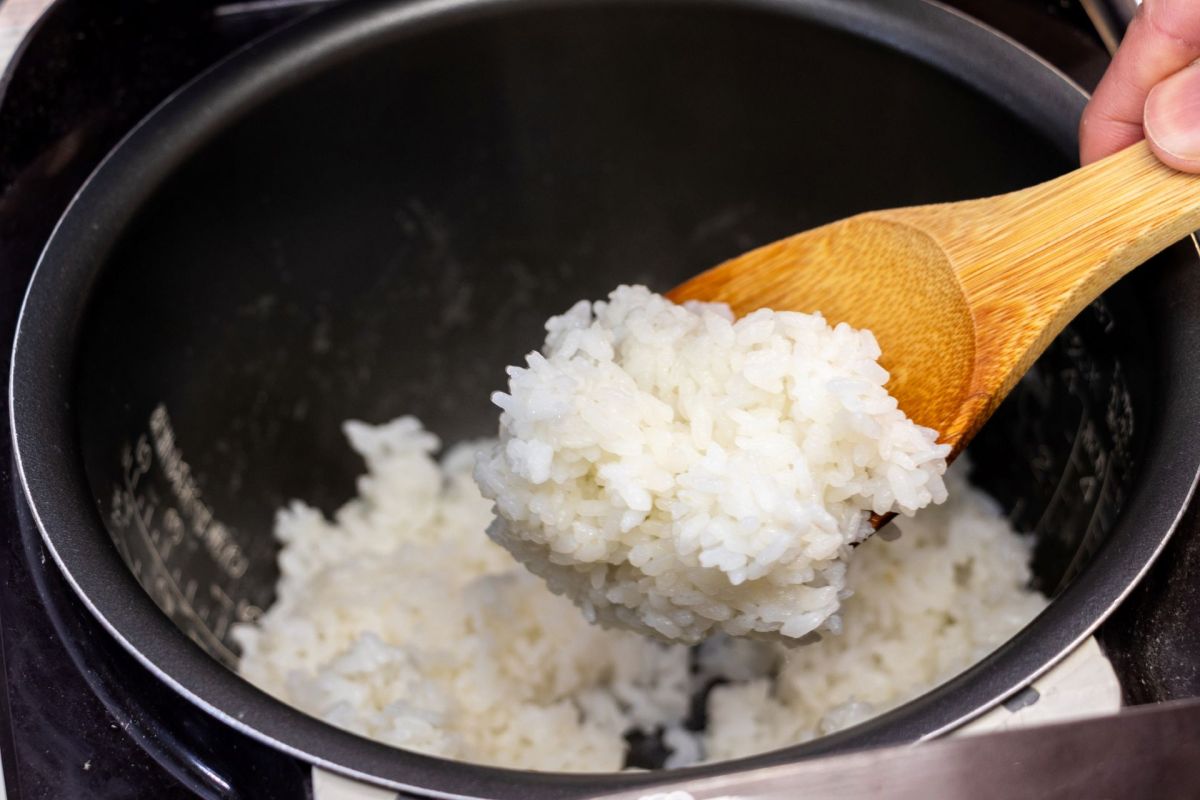 A person scooping rice from a rice cooker.