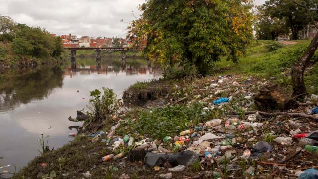 A polluted riverbank in Buenos Aires, Argentina, covered in litter and surrounded by plants and trees.