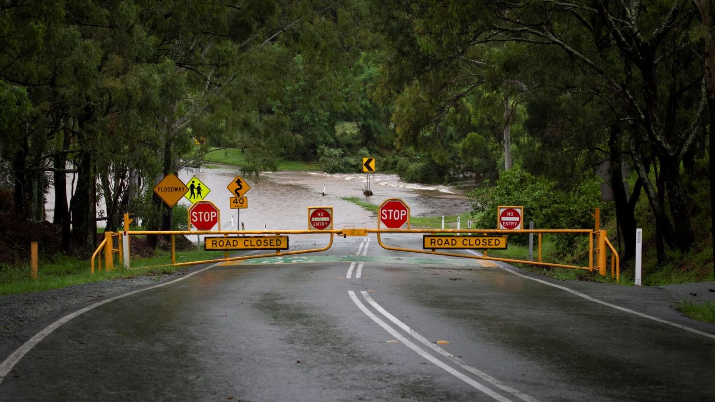 A yellow "road closed" gate and red stop signs block a road that is flooded.