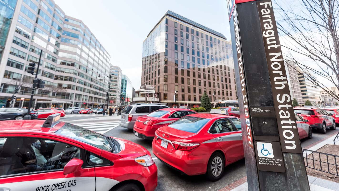 Red taxis and other vehicles are stopped at a crosswalk near Farragut North Station in Washington, D.C.