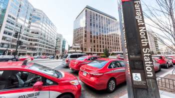 Red taxis and other vehicles are stopped at a crosswalk near Farragut North Station in Washington, D.C.