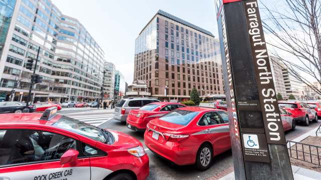 Red taxis and other vehicles are stopped at a crosswalk near Farragut North Station in Washington, D.C.