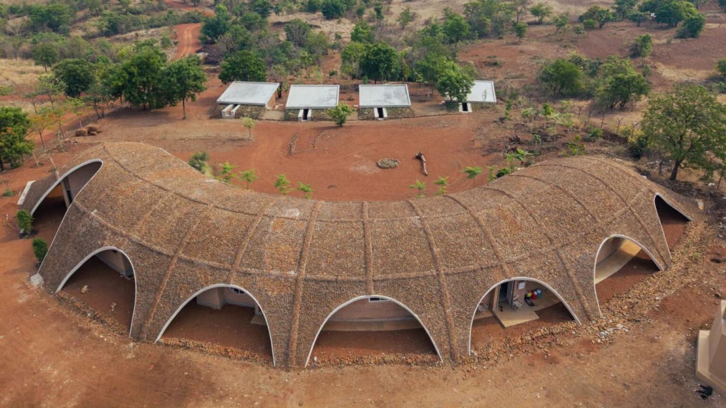 An aerial view of a uniquely designed building with a curved, rocky roof in a rural landscape.