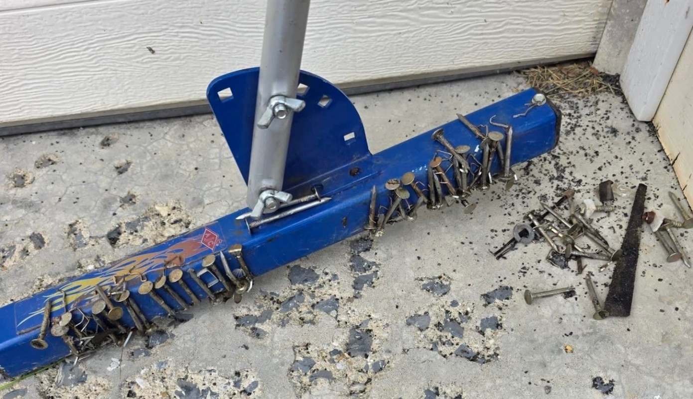 A blue tool with nails attached rests on a concrete surface alongside scattered metal fasteners.