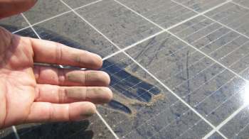 A hand with dirt on the fingers is positioned above a dusty solar panel.