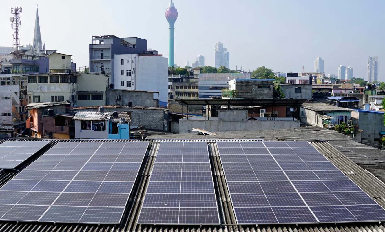 Solar panels installed on rooftops in Colombo, Sri Lanka, with the background featuring a telecommunications tower.