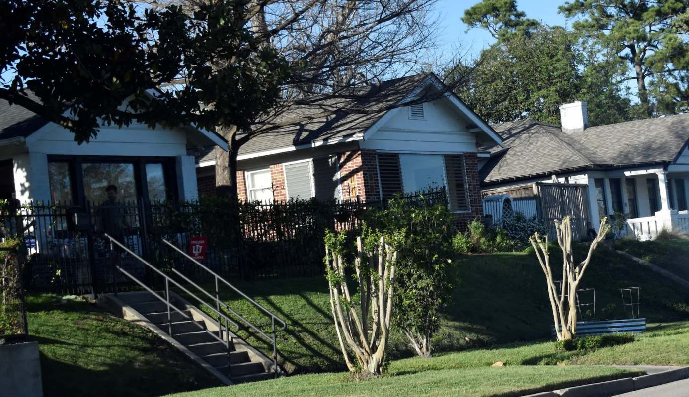 A row of houses with a grassy slope and a set of stairs leading to a fenced porch area.