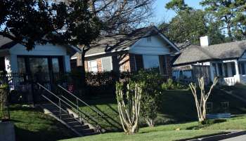 A row of houses with a grassy slope and a set of stairs leading to a fenced porch area.