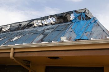 A damaged roof covered with blue tarps and exposed areas under a partly cloudy sky.