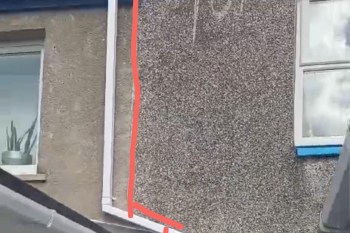 A textured wall with a window and a visible section of plumbing.
