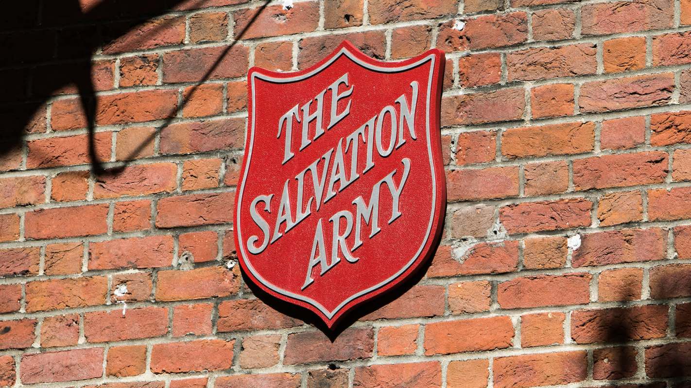 A red sign with "The Salvation Army" mounted on a brick wall.