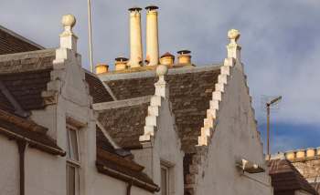 Rooftops of buildings in Scotland featuring decorative gables and various chimney types against a cloudy sky.