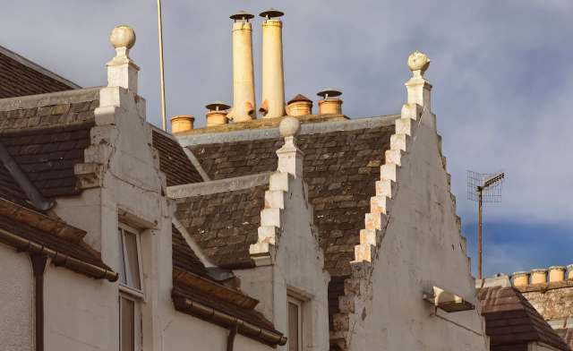 Rooftops of buildings in Scotland featuring decorative gables and various chimney types against a cloudy sky.