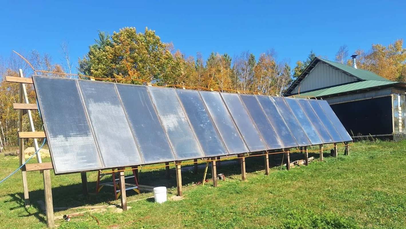 Solar panels installed on a structure in a field near a building with a green roof.