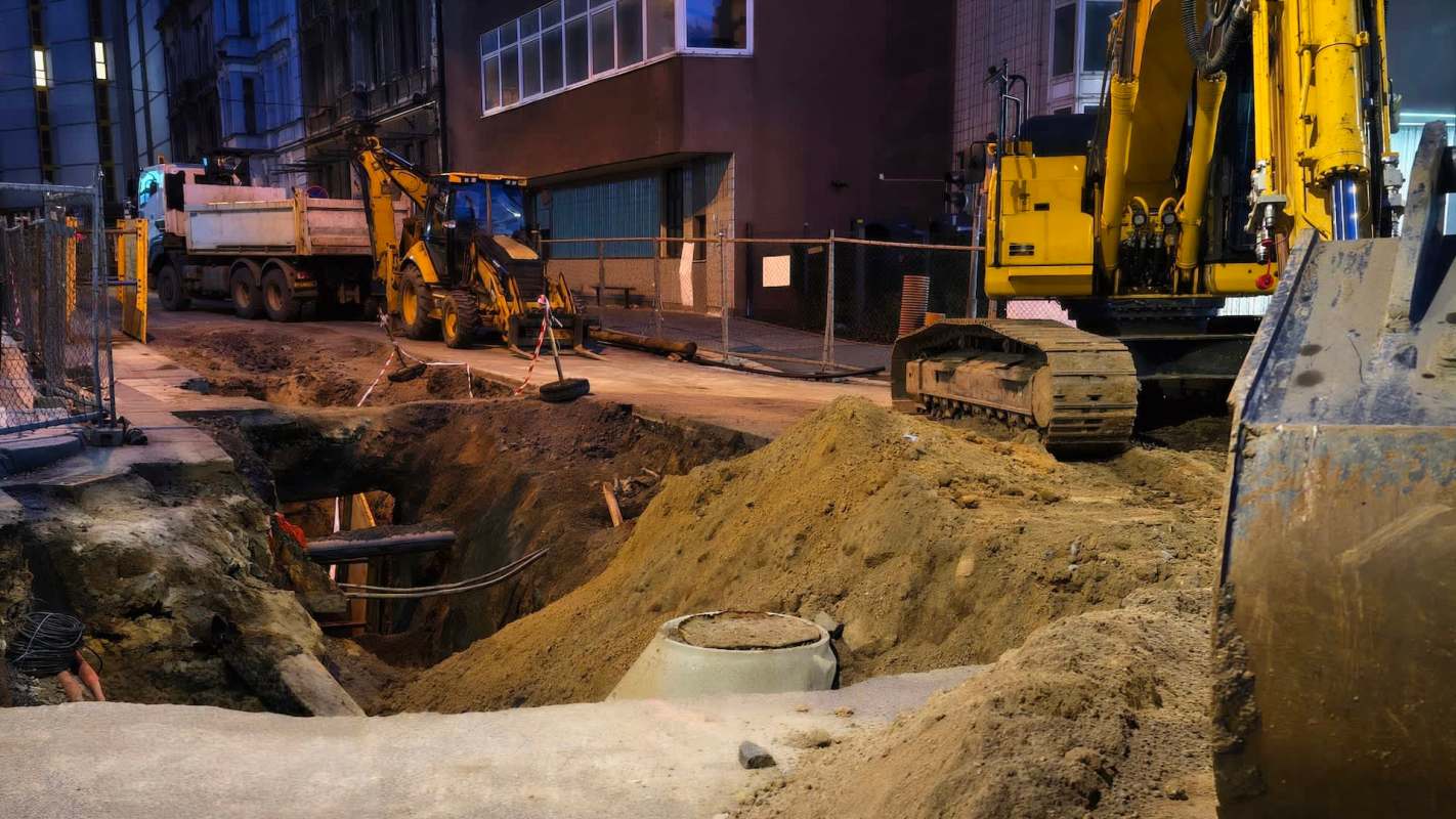 Construction site at night with heavy machinery and an excavation partially filled with dirt.