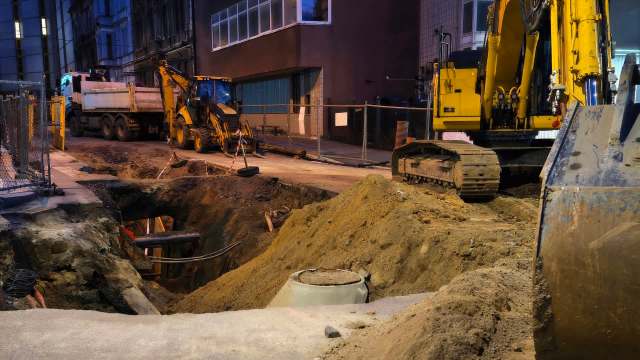 Construction site at night with heavy machinery and an excavation partially filled with dirt.