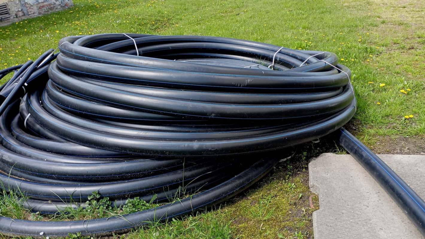 A coil of black tubing resting on grass near a concrete path.