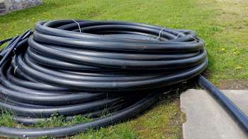 A coil of black tubing resting on grass near a concrete path.