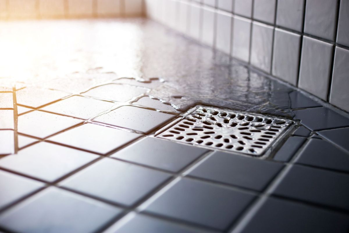 Water accumulates on tiled flooring near a shower drain.