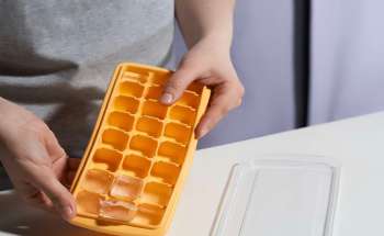 A person holds an orange ice cube tray with several ice cubes in it.
