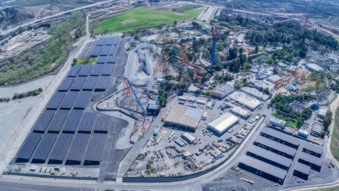 An aerial view of Six Flags Magic Mountain with roller coasters and a large solar panel installation nearby.