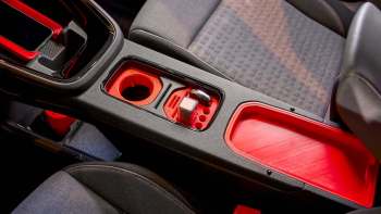 A car interior featuring a console with red accents, cup holders, and a storage compartment.