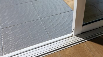 A sliding door threshold with textured gray tiles and wooden flooring.