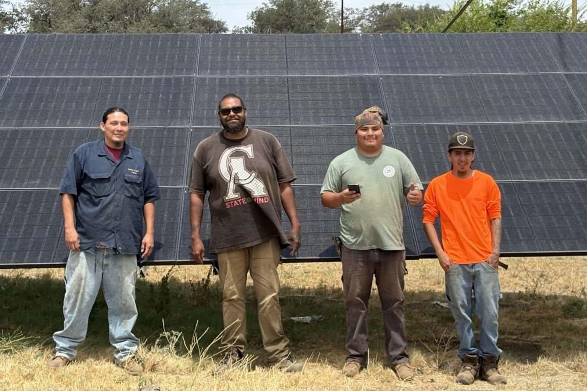 Four workers stand in front of a solar panel installation.