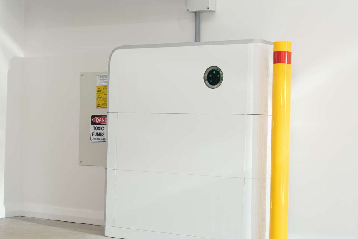 A white battery near a caution sign about toxic fumes in a white-walled space.