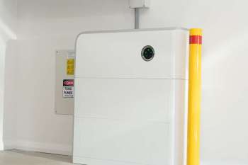 A white battery near a caution sign about toxic fumes in a white-walled space.