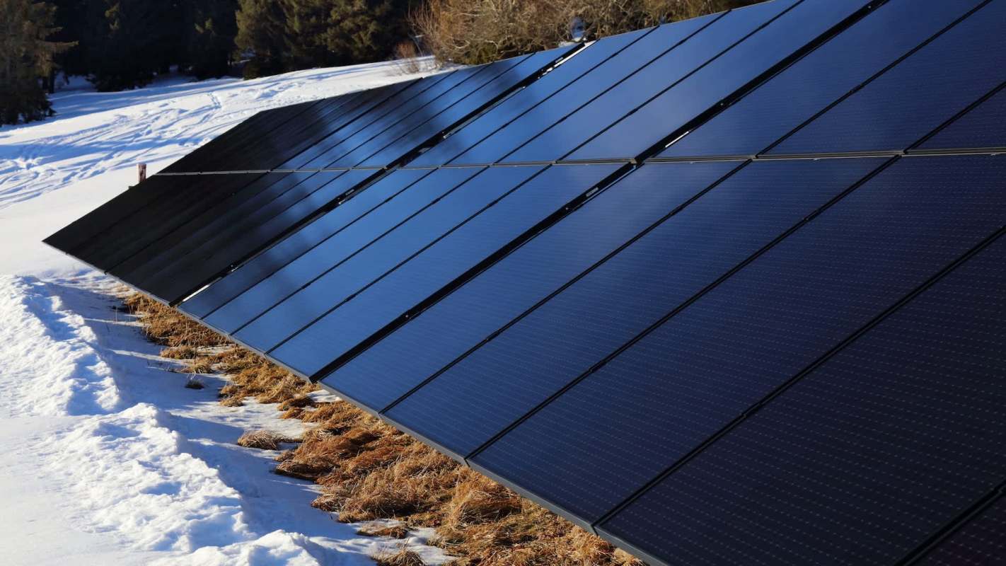Solar panels installed in a snowy environment with patches of brown grass.