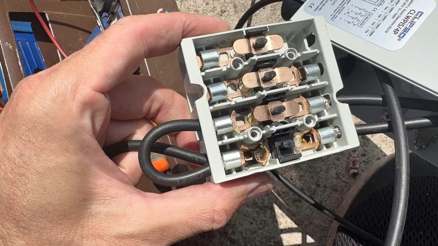 A person holds a gray electrical connector with multiple terminals and wiring.