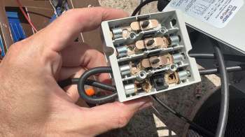 A person holds a gray electrical connector with multiple terminals and wiring.