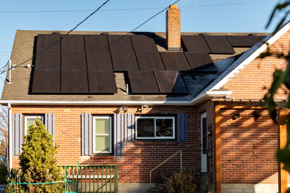 A house with solar panels on the roof and a brick exterior, featuring green shutters and a porch.