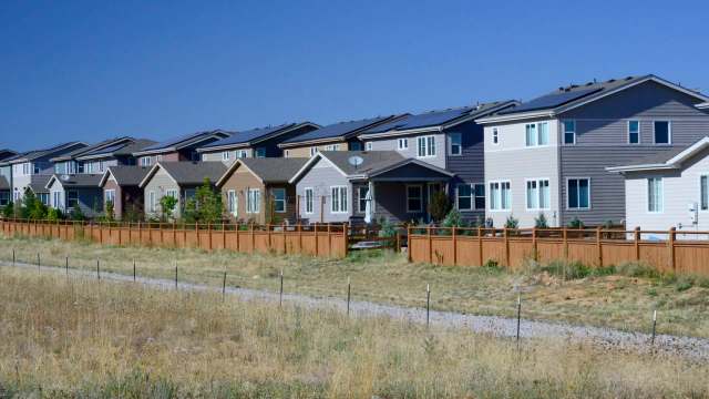 A row of residential houses with fences and solar panels, set against a clear blue sky.