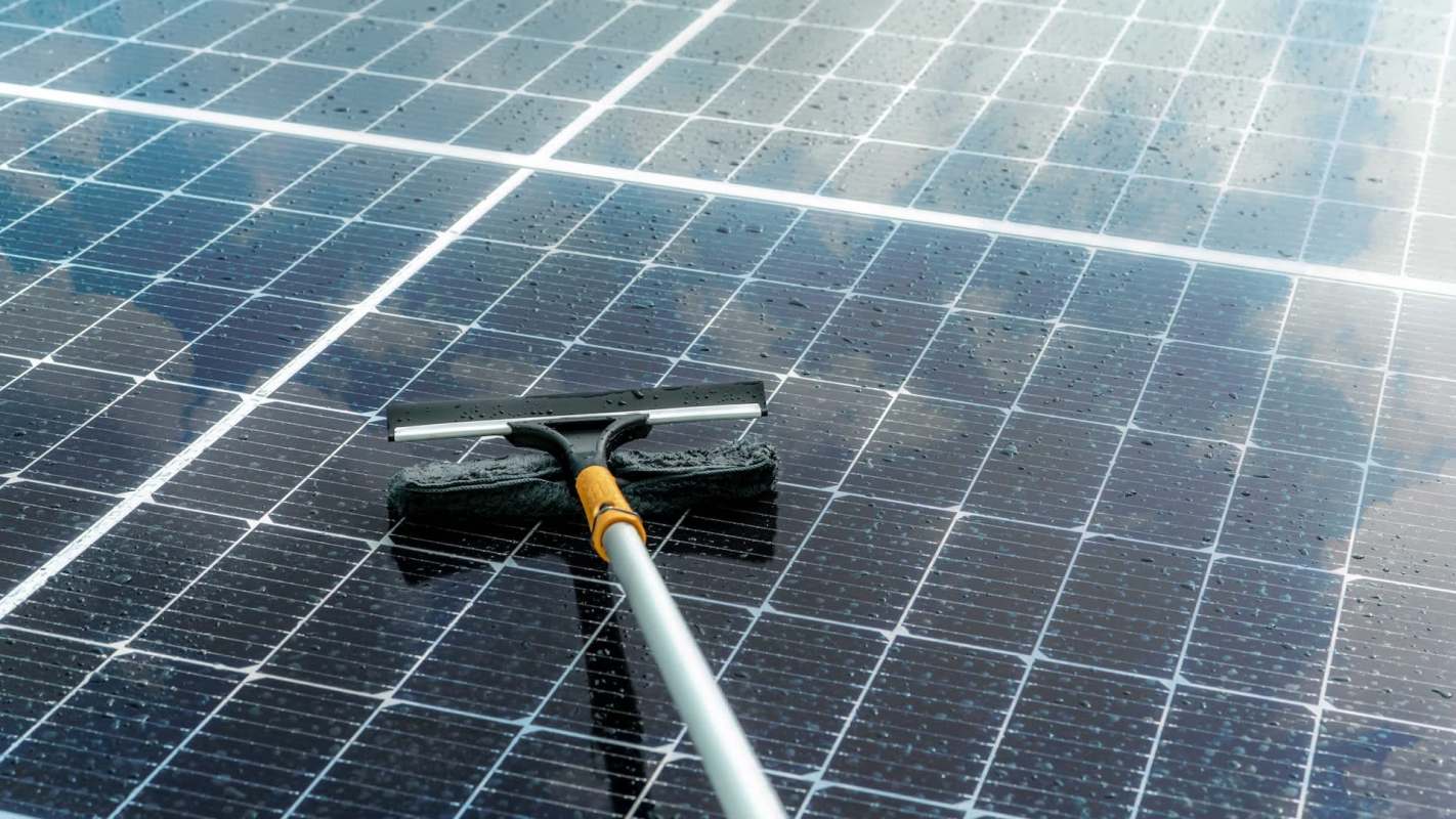 A squeegee resting on wet solar panels covered in water droplets.