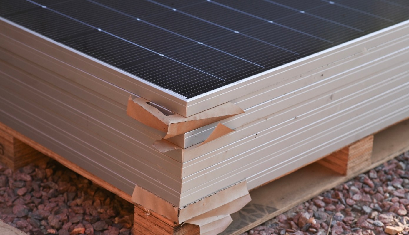 A stack of solar panels with packaging materials placed on wooden pallets.