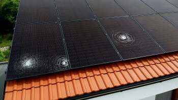 A solar panel roof with circular patterns, positioned above a red tiled roof.