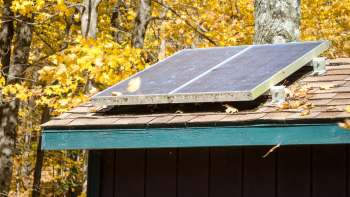 A solar panel installed on the roof of a cabin surrounded by autumn foliage.